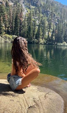 a woman sitting on top of a rock next to a lake