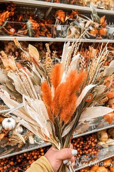 a person is holding some dried flowers in front of shelves with pumpkins and other autumn decorations