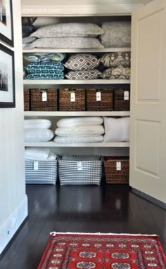 an organized closet with baskets, blankets and rugs on the floor in front of it