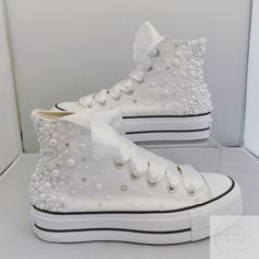 a pair of white high top sneakers with pearls and bows on the side, in a display case