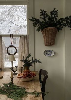 a wooden table topped with a basket filled with pine branches next to a window covered in curtains