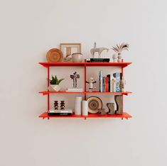 an orange shelf filled with books and knick knacks next to a white wall