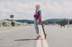 a woman standing on the side of a road holding a skateboard