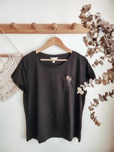 a black t - shirt hanging on a wooden hanger next to some dried plants