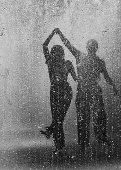 two people standing in the rain with their hands up to their head and one person holding an umbrella