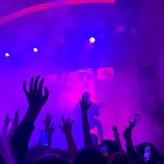 people raising their hands in the air at a concert with purple and pink lighting behind them