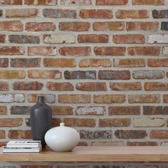 a white vase sitting on top of a wooden table next to a brick wall with a black bottle