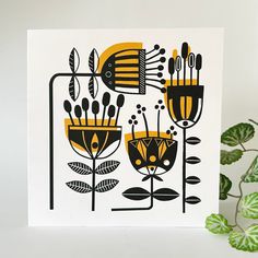 a white card with black and yellow designs on it next to a potted plant