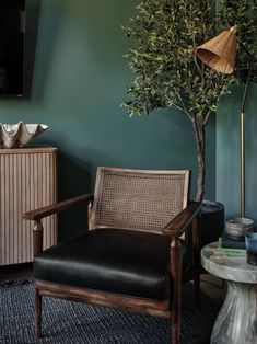 a living room with green walls and a chair next to a potted olive tree