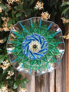 a glass bowl with blue and green designs on it sitting in front of some flowers