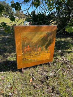 an old painting is sitting in the grass near some trees and bushes, it looks like there are people on horseback