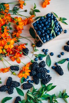 blueberries and orange flowers on a white surface with a box of berries in the middle