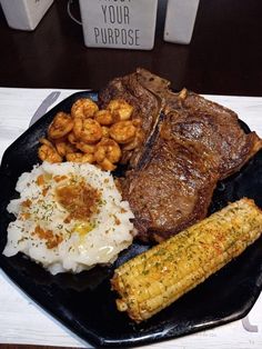 steak, mashed potatoes and corn on the cob are served on a black plate