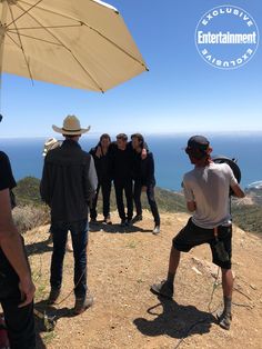 a group of people standing on top of a hill next to an umbrella over looking the ocean