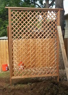 a wooden fence with lattice design in the yard next to a tree and trash can