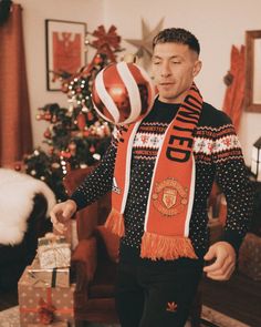 a man holding a ball in his hand while standing next to a christmas tree and presents