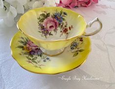 a yellow tea cup and saucer with flowers on it sitting next to pink roses