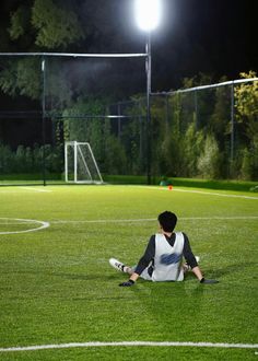 a person sitting on the ground in front of a soccer field at night with lights