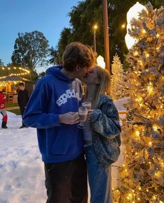 a man and woman kissing in front of a christmas tree with lights on the trees