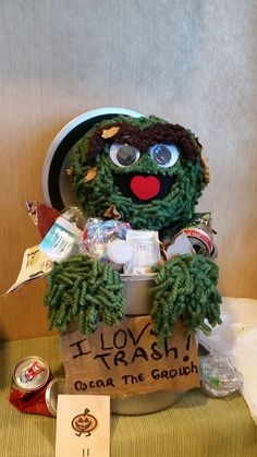 a green stuffed animal sitting on top of a table next to a sign that says i love trash oscar the grouch