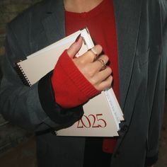 a woman in a red sweater holding a binder and a ring on her finger