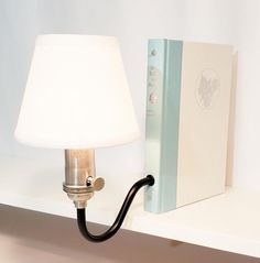 a lamp on a white shelf next to a book and a light blue box with a black handle