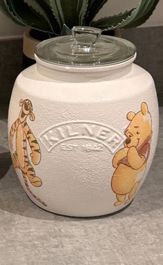 a white ceramic pot with winnie the pooh and tigger on it next to a cactus