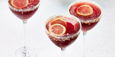 three wine glasses filled with red liquid and garnished with sugar, orange slices and sprinkles