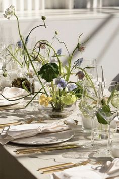 the table is set with white plates, silverware and flowers in glass vases