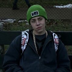 a young man wearing a green beanie sitting on a bench