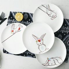 three plates with designs on them sitting next to a fork and knife, along with a slice of lemon