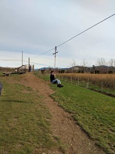 a person sitting on the ground in front of an open field with grass and power lines