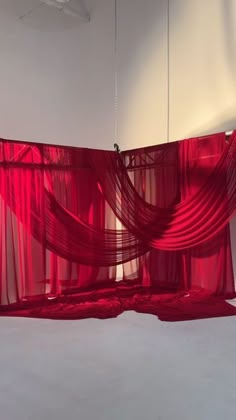 a red curtain hanging from the ceiling in a room with white walls and flooring