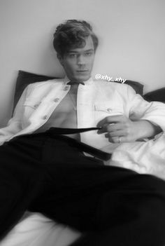 a black and white photo of a man in a suit sitting on a bed holding a tie