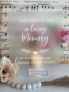 this candle burns in loving memory sign with flowers and beads on the table next to it