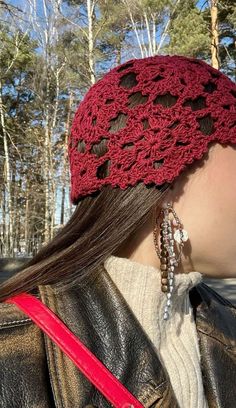 a woman wearing a red crochet hat with long hair and earrings on her head