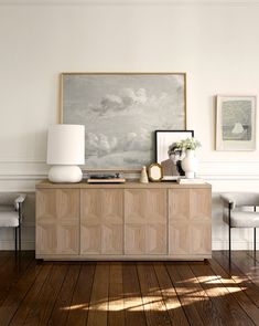 a living room with white walls and wood flooring on the sideboard, two chairs and a painting