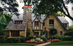 a stone house surrounded by trees and flowers