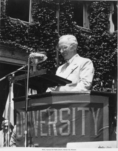 an old man standing at a podium in front of a building