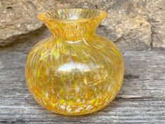 a yellow glass vase sitting on top of a wooden table next to a stone wall