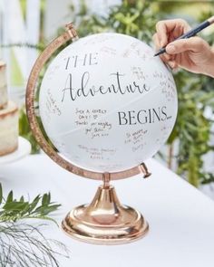 a person writing on a globe at a table with flowers and greenery in the background