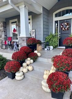 the front porch is decorated for fall with pumpkins and gourds in black planters