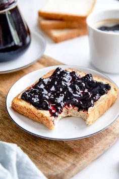 a piece of toast with blueberry sauce on it sitting on a plate next to a cup of coffee