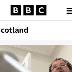 a man in glasses is standing next to the bbc scotland logo and has his hand out