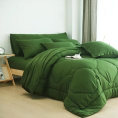 a bed with green comforters and pillows in a room next to a window,