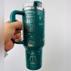 a person holding a green travel mug with the words harry potter on it and symbols