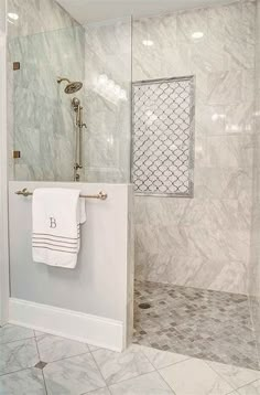 a bathroom with marble walls and flooring, white towels hanging on the shower door