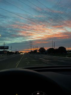 the sun is setting on an empty road with power lines in the distance and telephone poles above