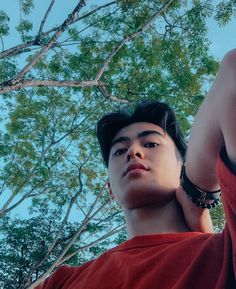 a young man standing in front of trees with his hand up to the sky above him