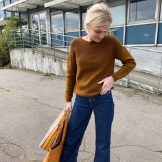 a woman is standing outside with her hand on her hip and holding shopping bags in her other hand